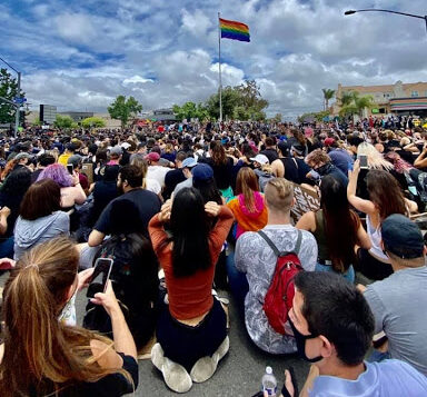 Large group of people kneeling in front of pride flag