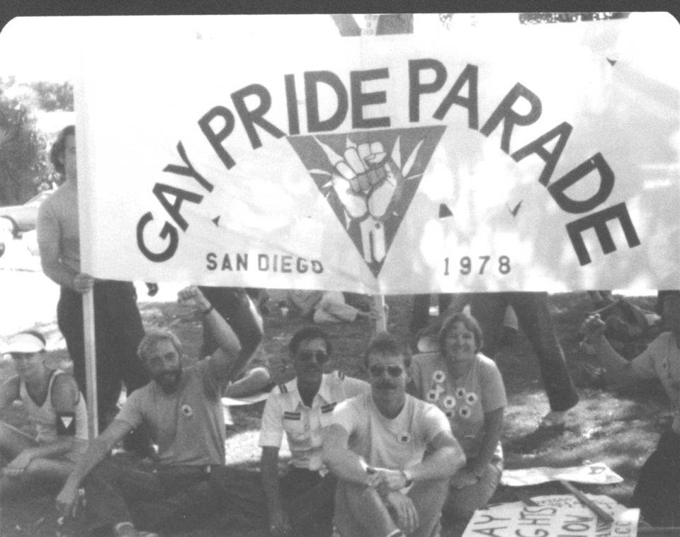 Black & white photo of people sitting under a banner that reads 