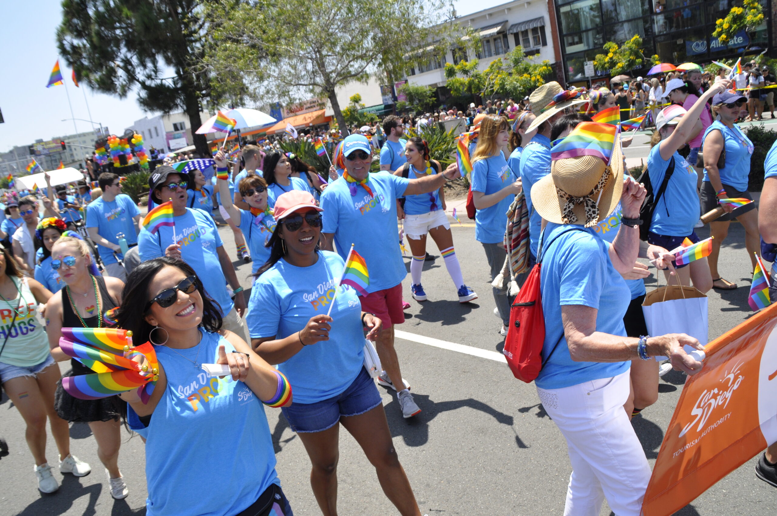 Group of people walking in Pride Parade with blue shirts and rainbow flags