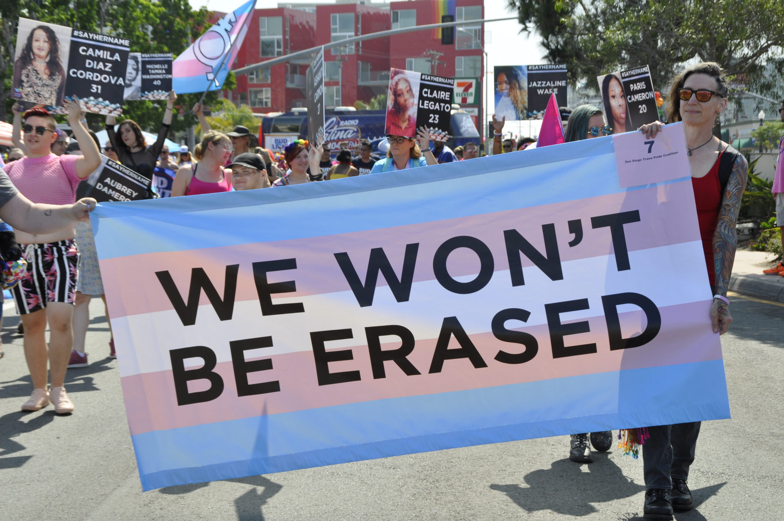 People holding banner with trans flag and words 