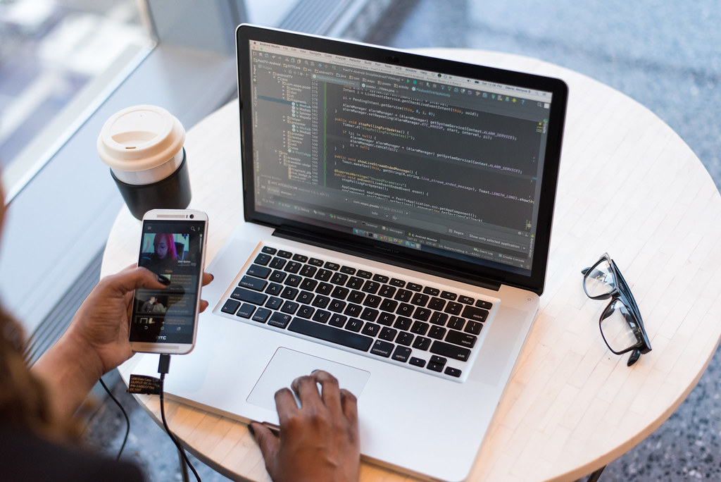 Person working on computer, holding cell phone, with coffee and glasses