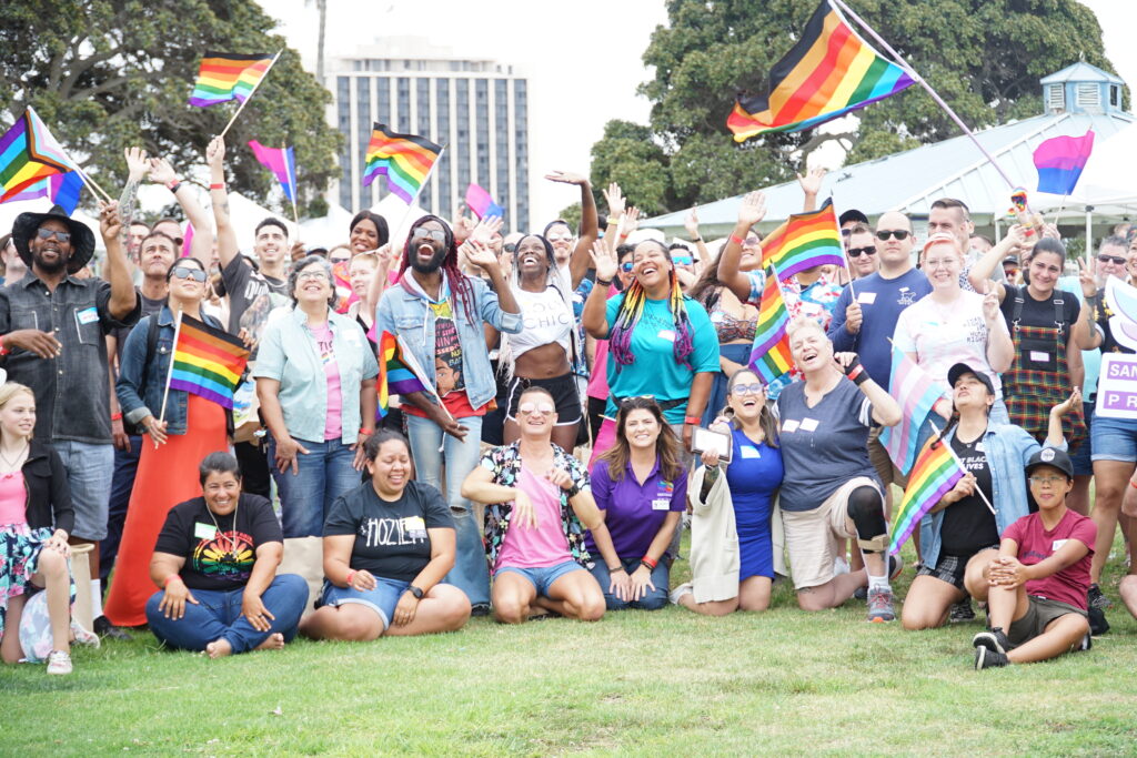 Large group of people waving and smiling with Pride flags